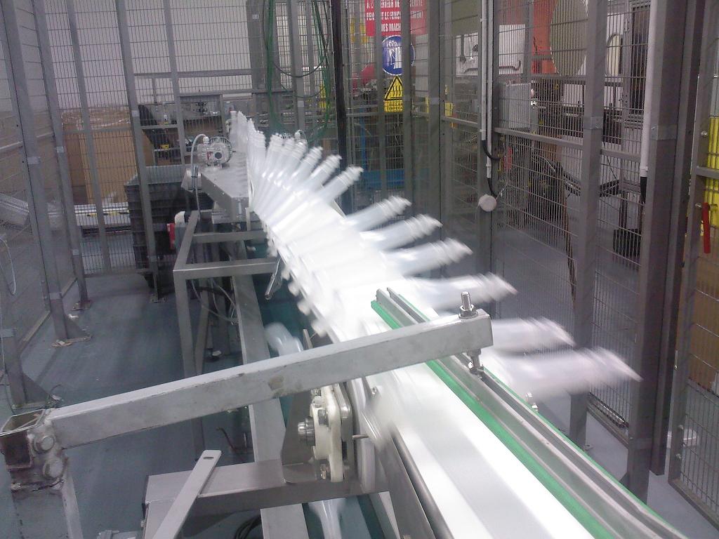 Convoyeur à bande pour retourner des bouteilles en plastique avec un système de découpe pour couperle surplus de plastique